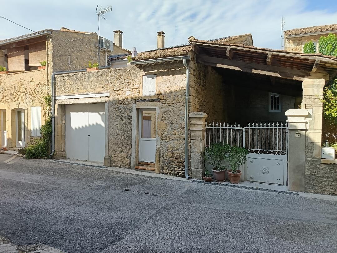 Un bâtiment en pierre avec un garage, une entrée fermée par un portail et une petite fenêtre.