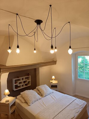 A bedroom with a bed, bedside tables, a lamp, a shelf with plants, and a window. - "The timeless": The Lodge near the Cèze. (Saint-André-de-Roquepertuis)