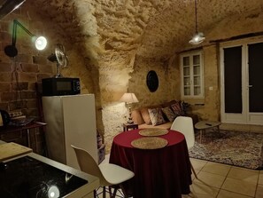 Ein gemütliches Zimmer mit Steinwand, einem Esstisch mit Stühlen, einer Couch und einem Fernseher.