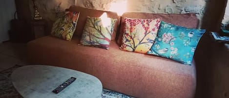 A cozy living area with a sofa, colorful cushions, a small round table, and a lamp.