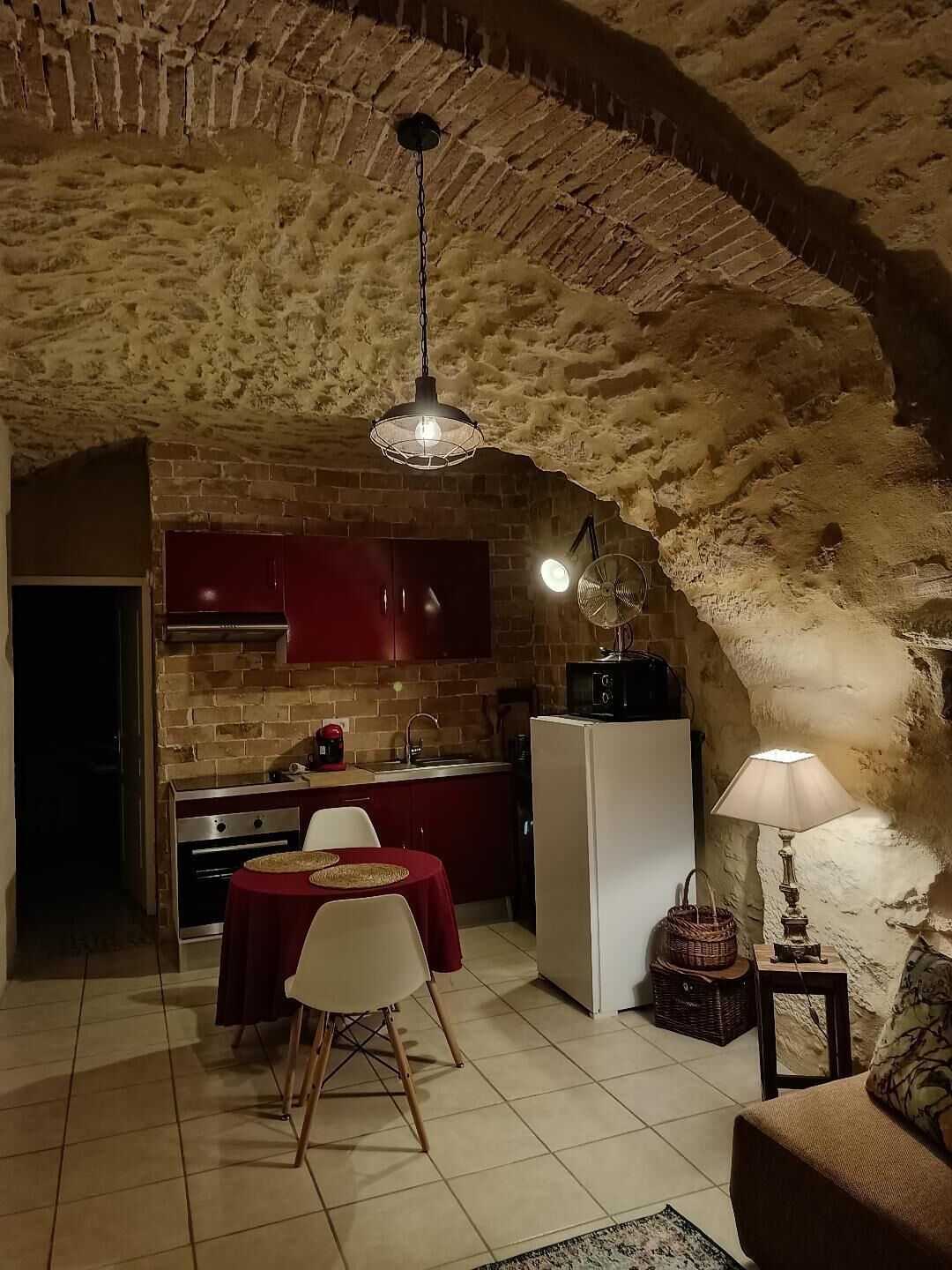 Una cucina accogliente con un arco in mattoni, un tavolo da pranzo con sedie, un frigorifero e una lampada.