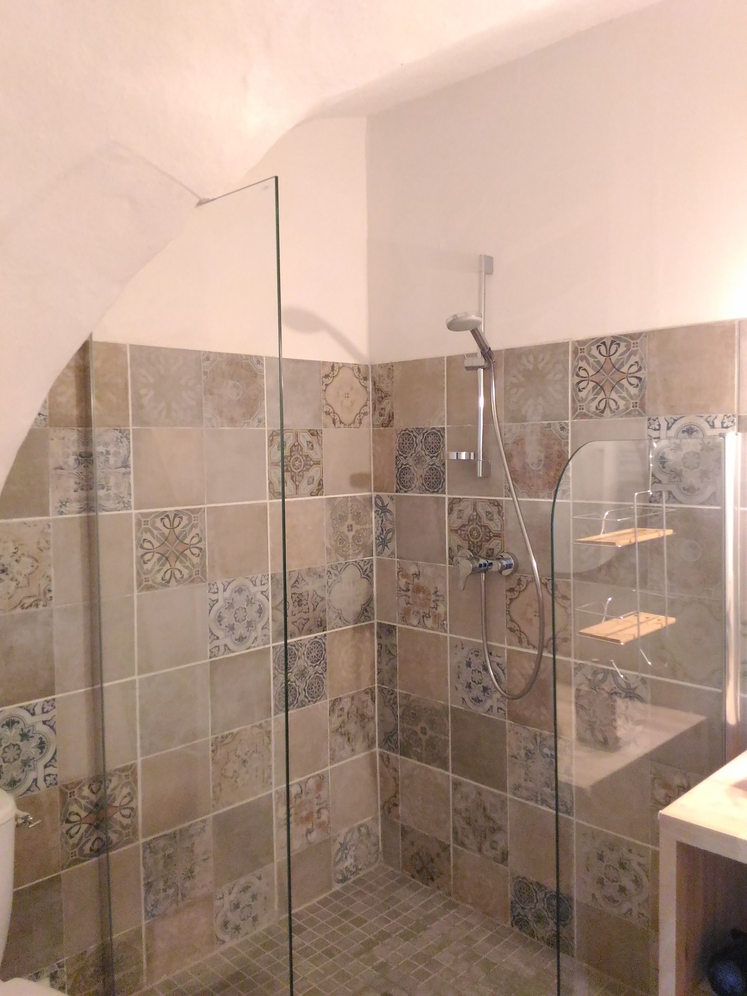 Un espace douche doté d’une porte en verre, de murs carrelés et d’un pommeau de douche.
