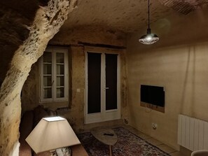 Ein Zimmer mit einer Steinsäule, einer Tür, einer Lampe, einem Fernseher und einem gemusterten Teppich.