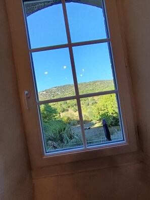 Ventana con vista despejada a un paisaje montañoso, un área cercada con vegetación y algunos objetos dispersos.