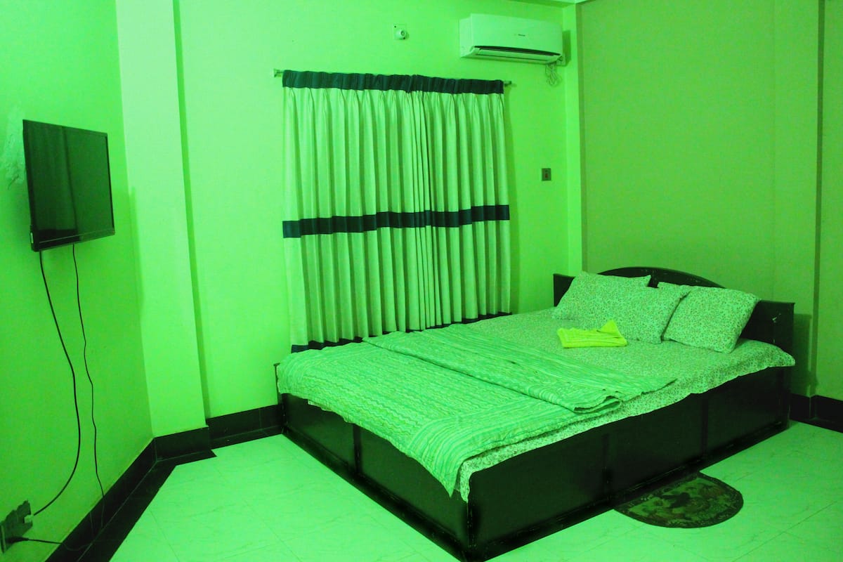 A room with a bed, a television mounted on the wall, and an air conditioning unit.