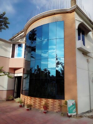 A building with a curved facade, large reflective glass windows, and a tiled ground floor. - Tony's Place (Sreemangal)