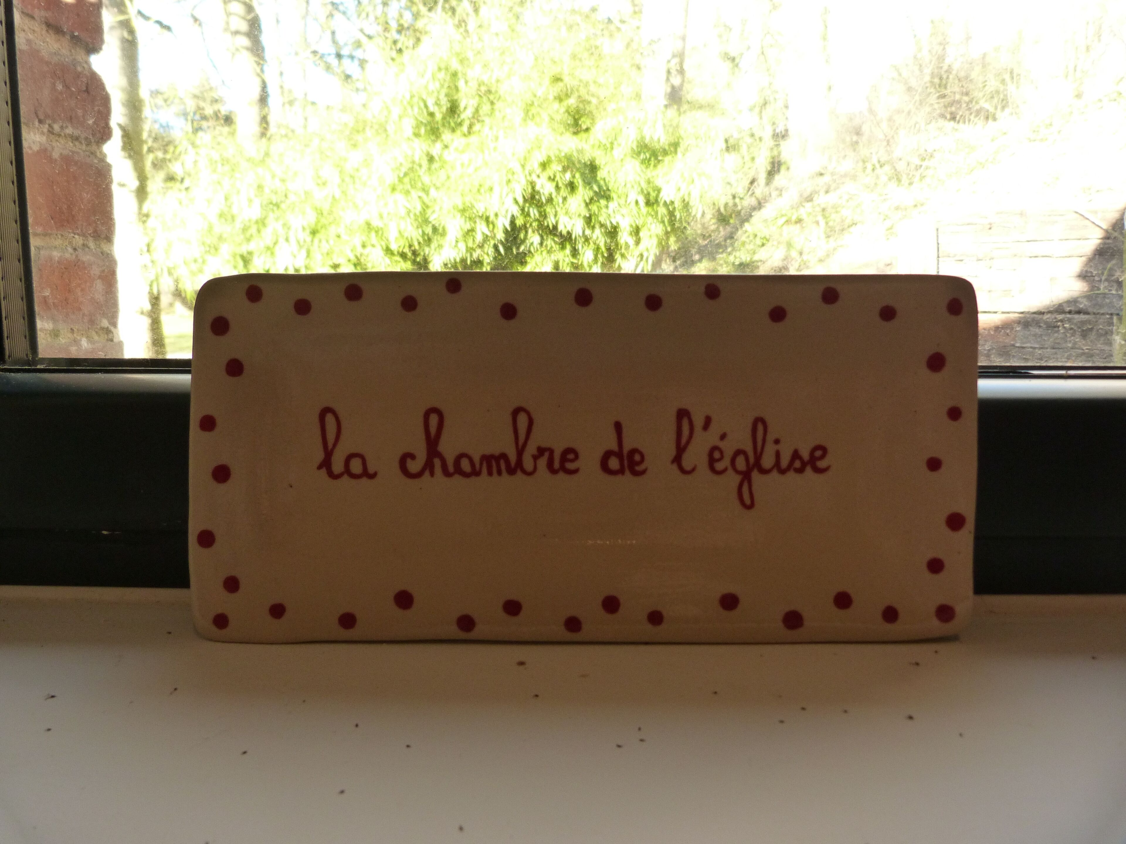 A wooden plaque with red dots and the text "la chambre de l'église" on a window sill.