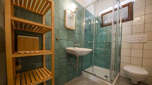 A bathroom with a wooden shelf unit, a sink, a glass-enclosed shower, and a toilet.