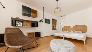 A modern room with a wooden floor, a brown woven chair, a white ottoman, a bed with two wicker headboards, and built-in shelves with various items.