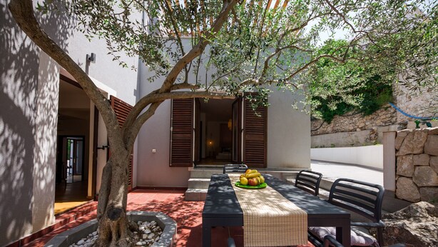 An outdoor dining area with a table and chairs, a tree, and a stone wall.