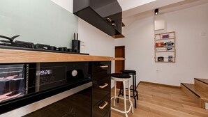 A modern kitchen with a built-in oven, a wooden countertop, and a black range hood. There are two black stools and a wooden table in the dining area.