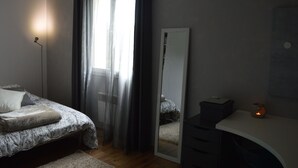 Een slaapkamer met een bed, nachtkastje, spiegel en raam met gordijnen.