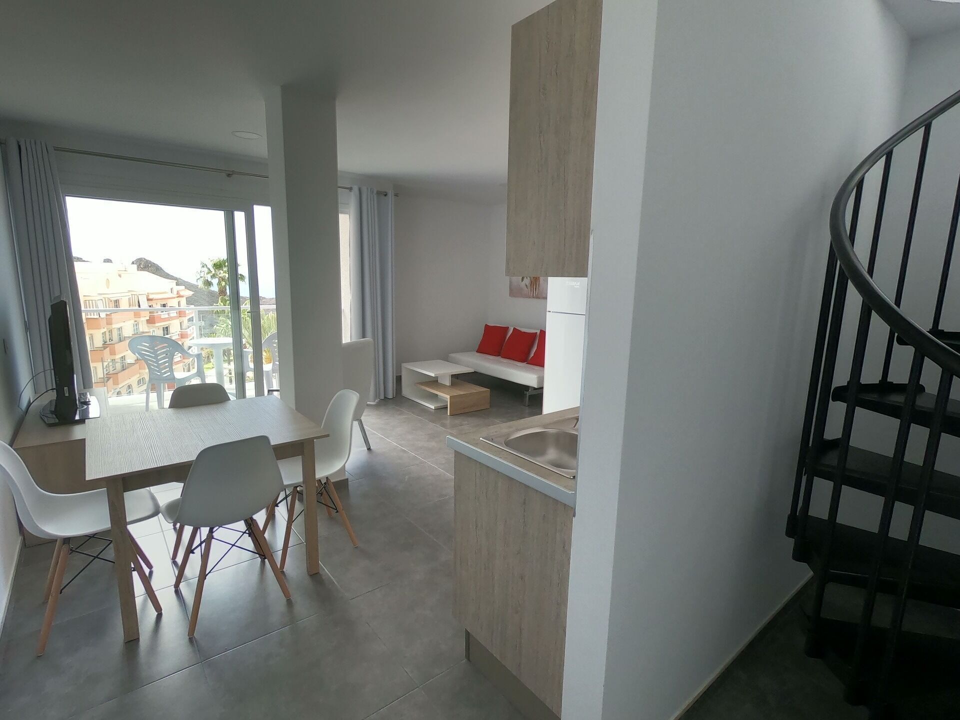 A modern apartment with a dining area, kitchen, and a staircase.