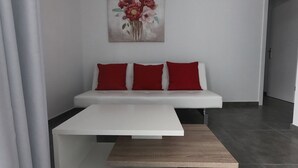 Ein modernes Wohnzimmer mit einem weißen Sofa, drei roten Kissen, einem Holztisch und einem Blumenbild an der Wand.