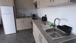 Eine moderne Küche mit Einbaukühlschrank, Spüle mit Wasserhahn und einer Arbeitsplatte, auf der ein Wasserkocher und eine Kaffeemaschine stehen.