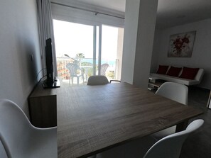 Et moderne værelse med et stort vindue, et spisebord, hvide stole, en sofa og et billede på væggen.