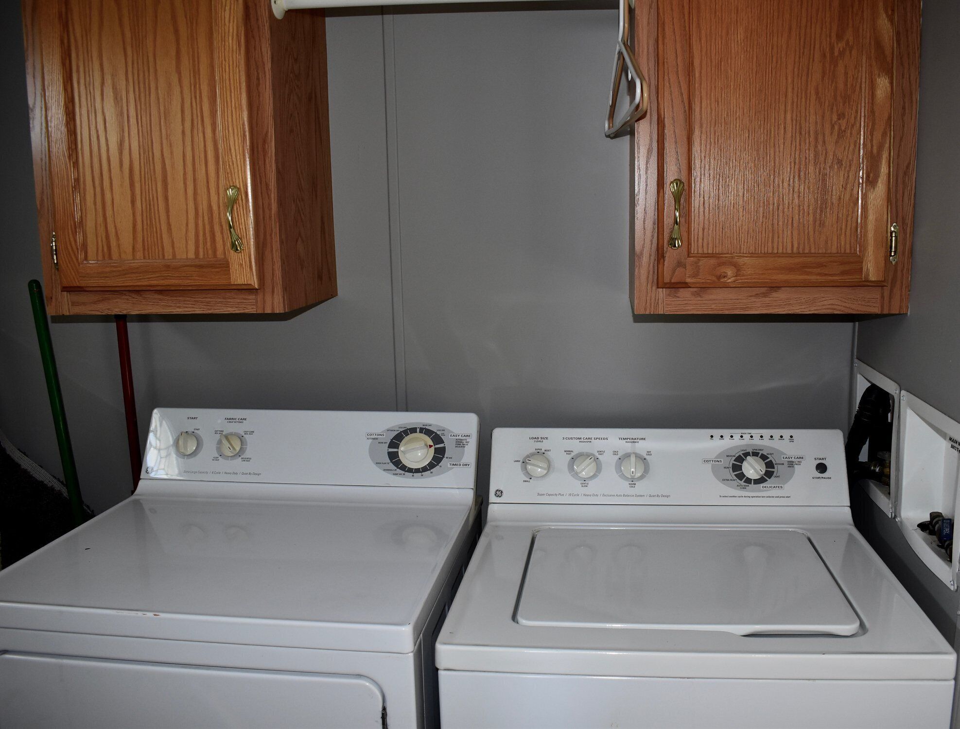 Two front-loading washers with control panels, wooden cabinets above, and a green broom leaning against the wall.