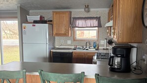 A kitchen with wooden cabinets, a refrigerator, a coffee maker, and a dining area with wooden chairs. - Lake Winnebago Vacation Rentals (Neenah)