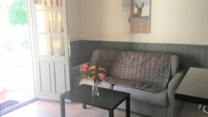 Un salon avec un canapé gris, une petite table noire ornée d’un vase de fleurs et une porte avec des rideaux.