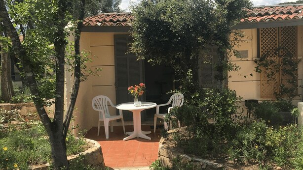 Une petite terrasse avec une table ronde et deux chaises, entourée de verdure et bordée d’un bâtiment dont le toit est recouvert de tuiles.