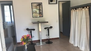 Une pièce avec une petite table, deux tabourets de bar noirs, un tableau encadré au mur, un vase avec des fleurs et un rideau sur le côté droit.