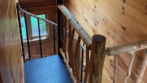 Un escalier en bois avec un puits de lumière, une rampe en métal et un sol bleu à texture.