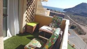 A balcony with a table, two chairs, a small wooden cabinet, and a view of the sea and hills. - Apartment in Cabo de Palos (Cabo de Palos)
