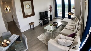 En moderne stue med sofa, fjernsyn og spiseområde med et glasbord.