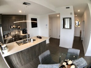 A modern kitchen with a central island, stainless steel appliances, and a glass dining table with chairs. - Stunning PENTHOUSE Top Floor 2 Bedrooms with breath taking view over Montreal / Laval (Ahuntsic CartierVille)