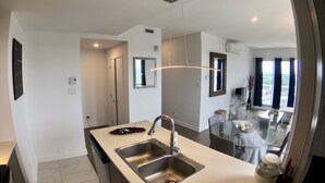 Et moderne køkken med en stor ø, stålvask og et spiseområde med et glasbord og stole.
