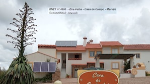 Una casa con techo de paneles solares, un letrero que dice "Casa do Castanheiro" y una planta grande en primer plano.