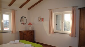 Un dormitorio con una cama, un aparador, un espejo y dos ventanas con cortinas.