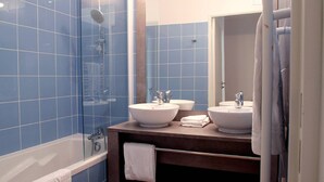 A bathroom with blue tiles, two sinks, a shower, and a bathtub. - Appartement charmant et sympa | Accès piscine (Cabourg)