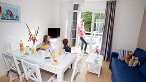 A bright living room with a dining area, a sofa with stuffed animals, and a painting on the wall. - Appartement charmant et sympa | Accès piscine (Cabourg)