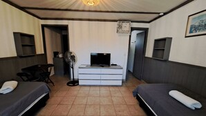 Een hotelkamer met twee bedden, een bureau met een televisie, een ventilator en een kleine kitchenette.