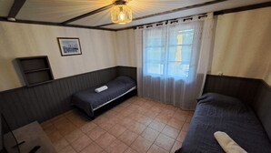 Een kleine, eenvoudige kamer met een bed, een klein tafeltje en een raam met gordijnen.
