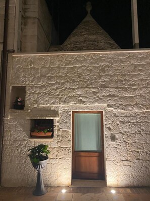 Un bâtiment en pierre avec une porte en bois et une petite fenêtre. Un pot de fleurs est placé devant la porte.