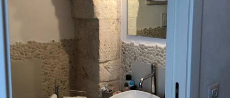 A bathroom with a stone arch, a sink, a mirror, and a towel rack.