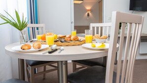 A breakfast table with croissants, orange juice, and a bowl of fruit. - Accès piscine ! Studio cosy et au calme ! (La Rochelle)