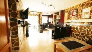 A spacious living area with a stone accent wall, a dining table with chairs, and a television mounted on the wall. - Finca basket, wheelchair accessible, stone villa by the sea. (Els Poblets)