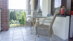 Ein Balkon mit Korbmöbeln, einem Glastisch und einem roten Feuerlöscher.