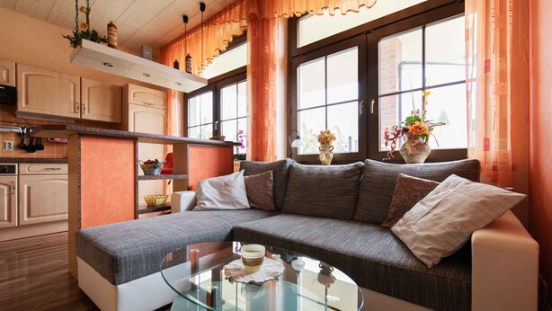 Ein modernes Wohnzimmer mit einem Glastisch, einer Couch und einer Küchenzeile im Hintergrund.