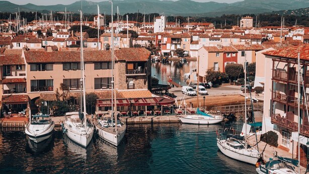 A marina with boats docked, buildings with red-tiled roofs, and a restaurant named 'RESTAURANT PIZZERIA.' - Super endroit ! Joli Studio équipé près du Port (Grimaud)