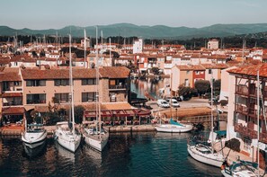 Un puerto deportivo con barcos amarrados, edificios de techo rojo y un restaurante llamado 'RESTAURANT PIZZERIA'.