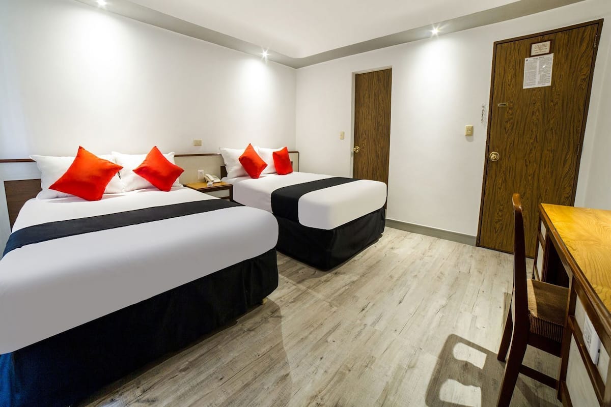 A hotel room with two beds, a desk, and a wooden door.