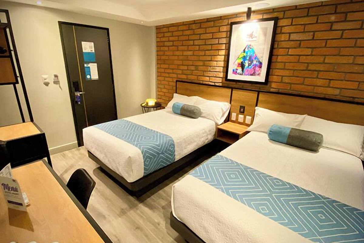 A hotel room with two beds, a desk, and a brick wall.