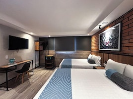 Une chambre d’hôtel moderne, équipée de deux lits, d’un bureau, d’une chaise, d’une télévision et d’un grand tableau accroché au mur.