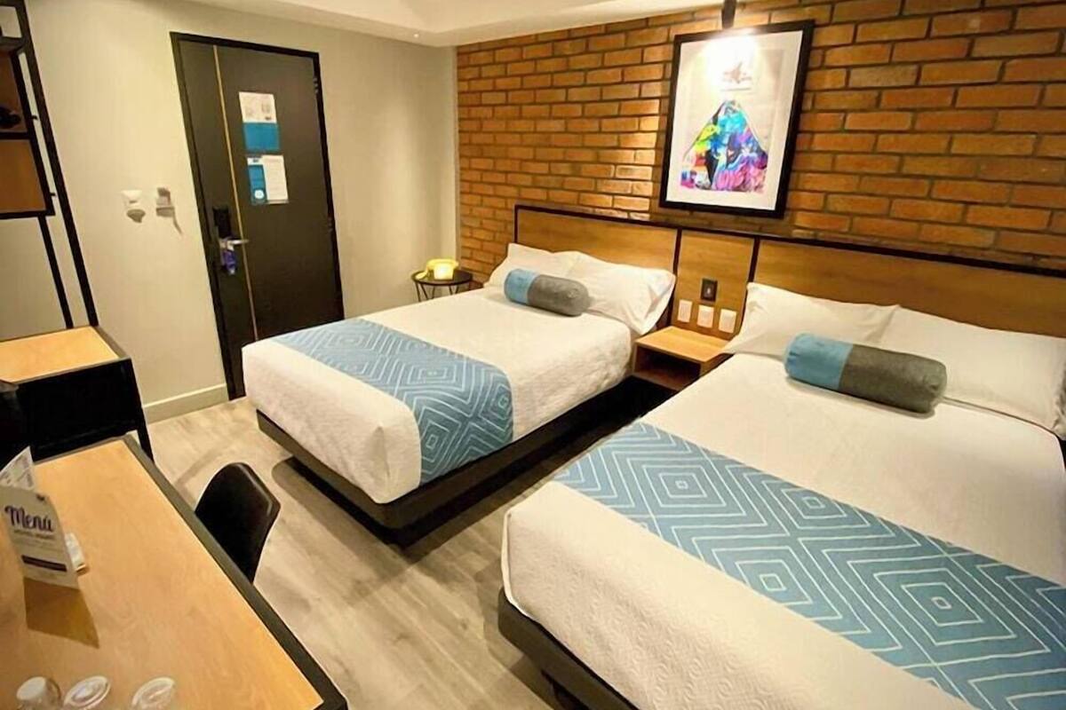 A hotel room with two beds, a wooden headboard, a brick wall, and a framed picture.