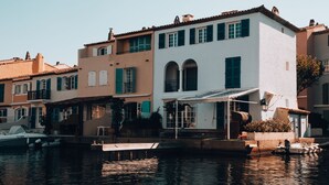A waterfront property with a white building, green shutters, and a boat docked in front. - Accès Piscines ! Appartement cosy et charmant (Grimaud)