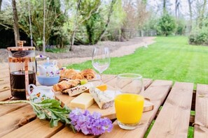 Un montaje para picnic con comida y bebidas sobre una mesa de madera, rodeado de follaje.